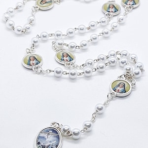 May include: White pearl rosary with silver medallions featuring images of the Virgin Mary and Jesus Christ. The rosary has a crucifix pendant.