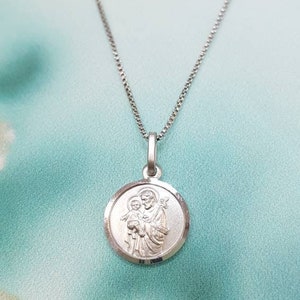May include: A silver chain necklace with a round pendant featuring a depiction of Saint Joseph holding the baby Jesus.