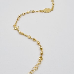 May include: A gold-toned rosary bracelet with a small cross charm and a round pendant. The bracelet is made of small gold beads and a chain.