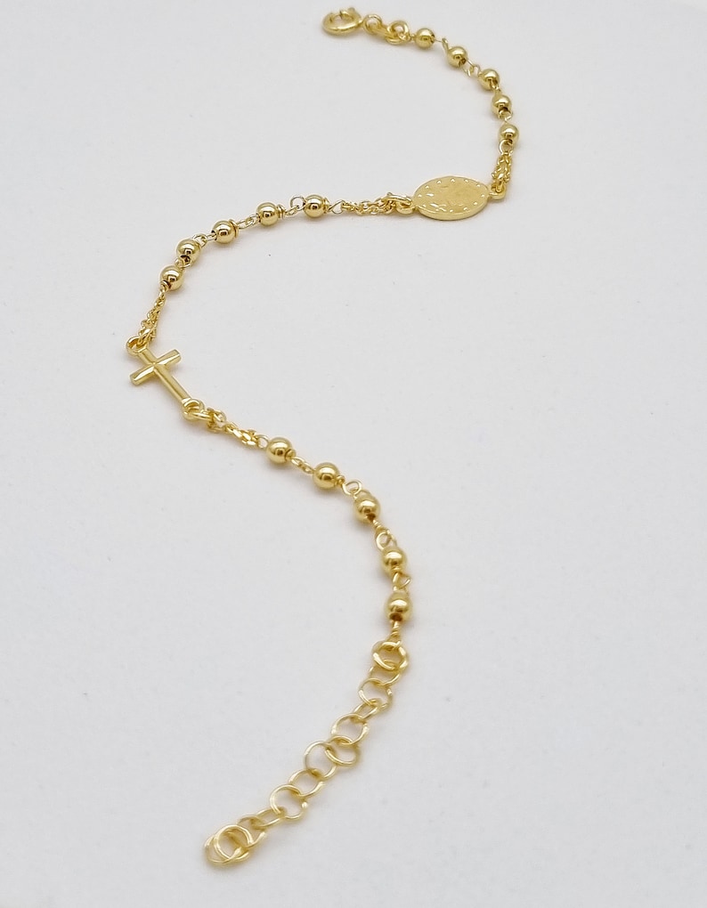 May include: A gold-toned rosary bracelet with a small cross charm and a round pendant. The bracelet is made of small gold beads and a chain.