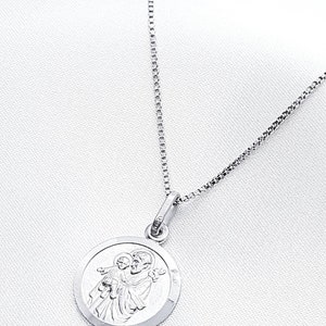 May include: A silver chain necklace with a round pendant featuring a detailed image of Saint Anthony of Padua holding a baby Jesus.