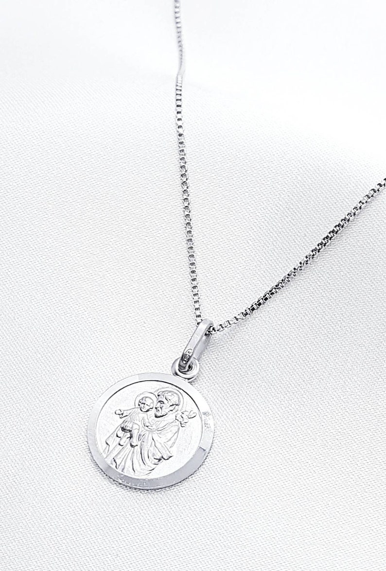 May include: A silver chain necklace with a round pendant featuring a detailed image of Saint Anthony of Padua holding a baby Jesus.