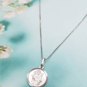 May include: A silver chain necklace with a round pendant featuring a depiction of the Holy Family. The pendant has a raised edge and a smooth, polished finish.