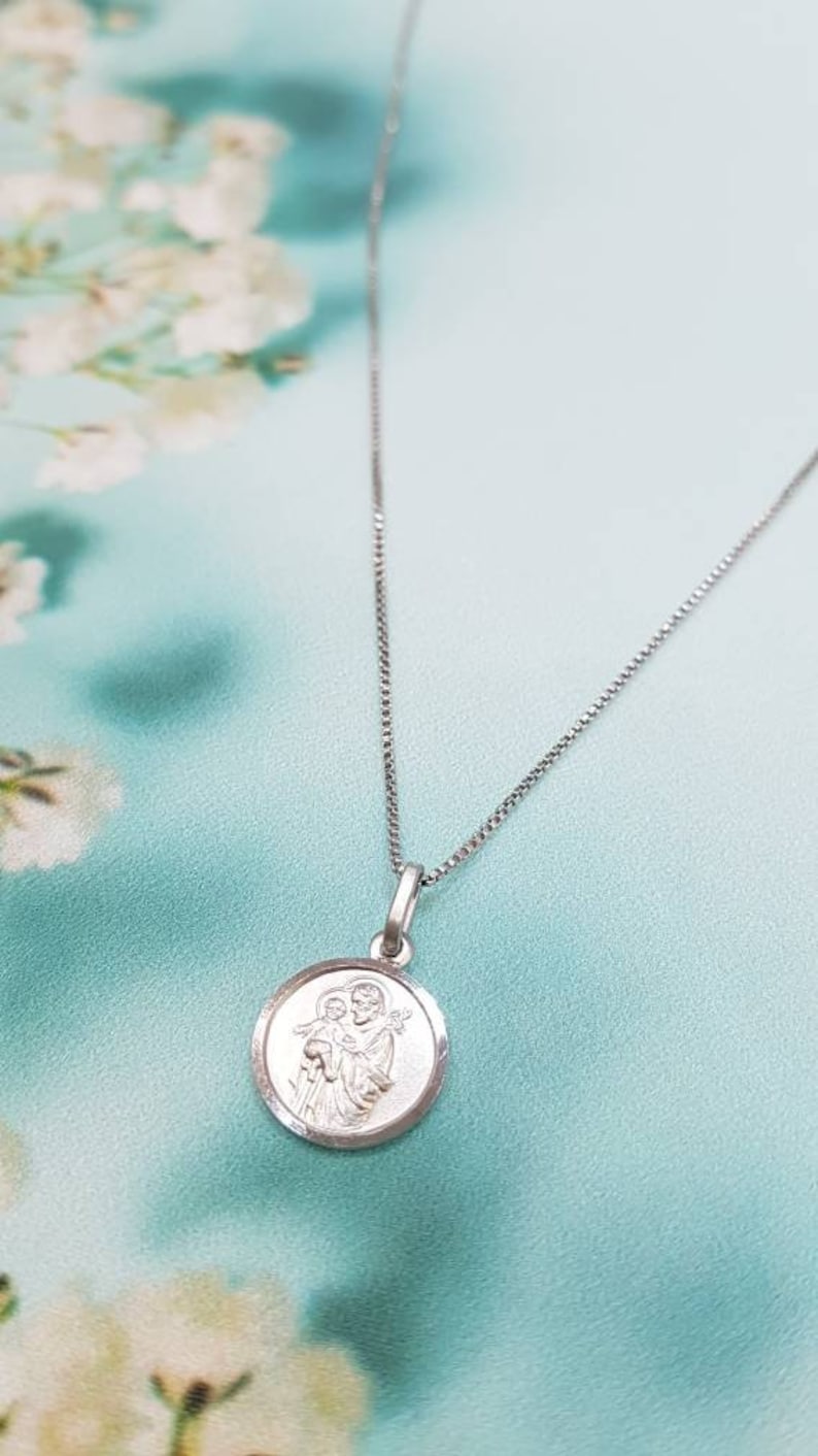 May include: A silver chain necklace with a round pendant featuring a depiction of the Holy Family. The pendant has a raised edge and a smooth, polished finish.