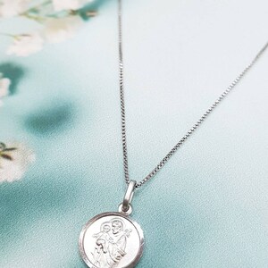 May include: A silver chain necklace with a round pendant featuring a silver image of Saint Anthony of Padua holding a baby Jesus.