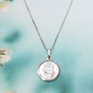 May include: Silver chain necklace with a round pendant featuring a depiction of Saint Anthony of Padua holding a baby Jesus.