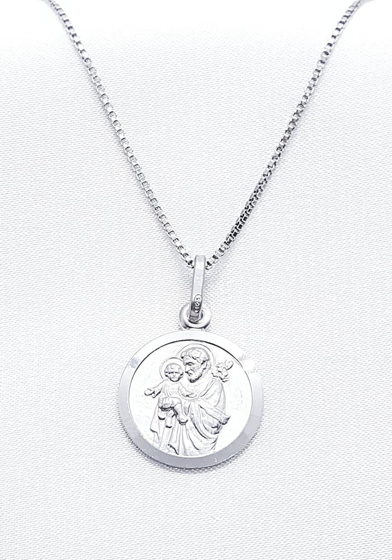 May include: A silver chain necklace with a round pendant featuring a depiction of Saint Anthony holding a baby Jesus.