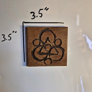 May include: Square wooden plaque, 3.5 inches by 3.5 inches, with a carved geometric design. The design features circles and triangles. The wood has a natural brown color.
