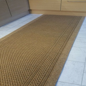 May include: A brown woven runner rug with a textured pattern and three raised stripes. The rug is made of natural fibers and has a rustic look.