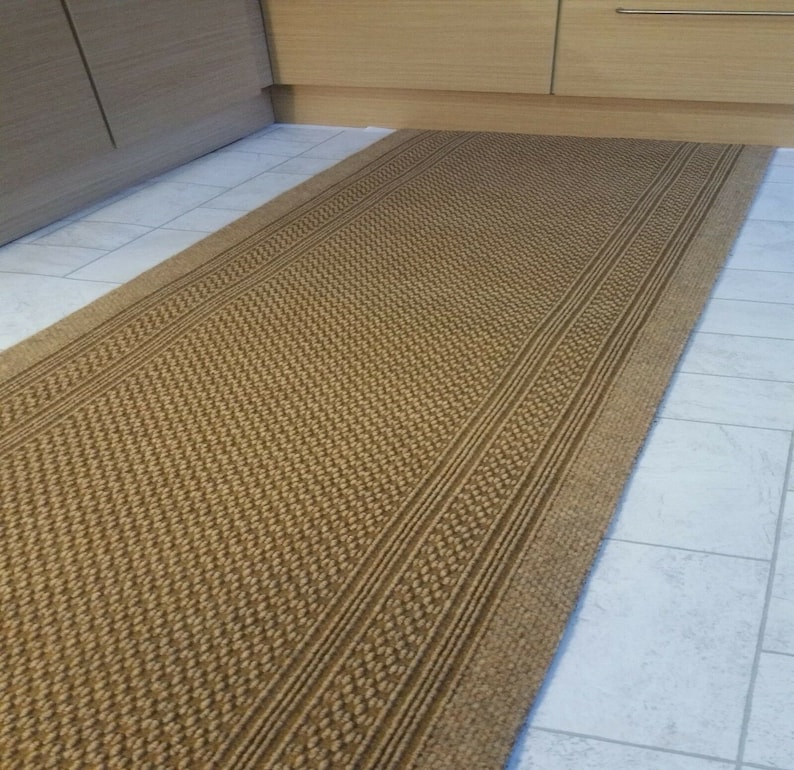 May include: A brown woven runner rug with a textured pattern and three raised stripes. The rug is made of natural fibers and has a rustic look.