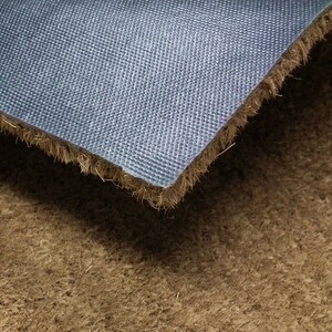 May include: Close-up of the back of a coir doormat. The mat has a blue rubber backing with a textured surface.