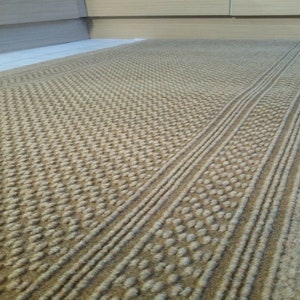 May include: A beige woven rug with a textured pattern. The rug has two rows of raised dots running down the center.