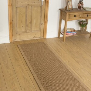 May include: A brown woven runner rug with a textured pattern. The rug is placed on a light wood floor in a hallway.