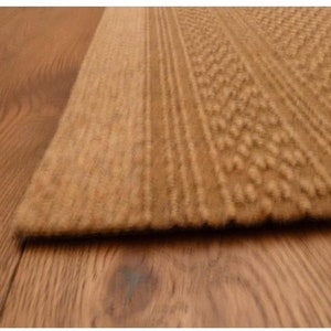 May include: Close-up of a brown textured rug with a subtle pattern. The rug has a thick pile and a soft, fuzzy texture.