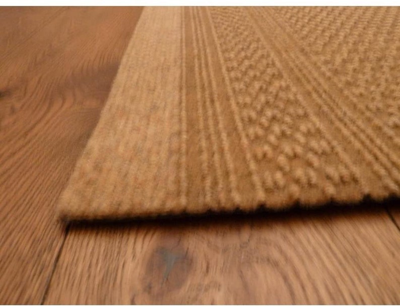 May include: Close-up of a brown textured rug with a subtle pattern. The rug has a thick pile and a soft, fuzzy texture.