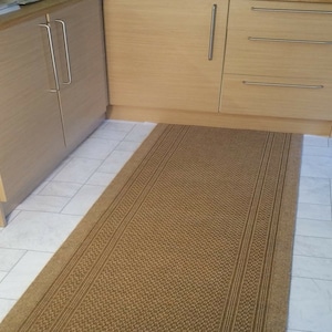May include: A brown woven rug with a textured pattern. The rug is placed in front of a set of wooden cabinets with silver handles.