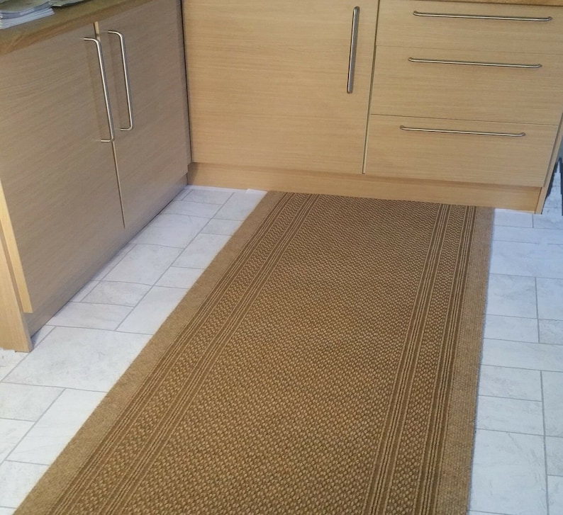 May include: A brown woven rug with a textured pattern. The rug is placed in front of a set of wooden cabinets with silver handles.
