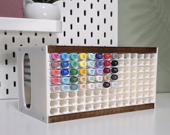May include: A white and brown marker organizer with multiple compartments. The organizer is filled with colorful markers, each labeled with a unique code. The wooden frame adds a touch of warmth to the design. The organizer is designed to hold a large collection of markers.