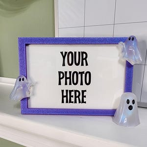 May include: Purple glitter picture frame with a white background and the text "Your photo here". Three white ghost figurines are attached to the frame.