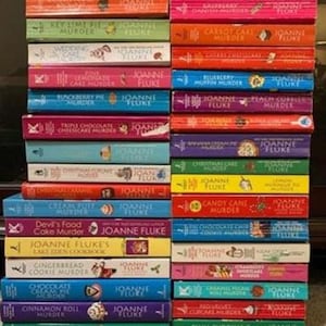 May include: A stack of colorful paperback books by Joanne Fluke, featuring titles like "Key Lime Pie Murder," "Carrot Cake Murder," and "Triple Chocolate Cheesecake Murder." The books have various colors and designs.