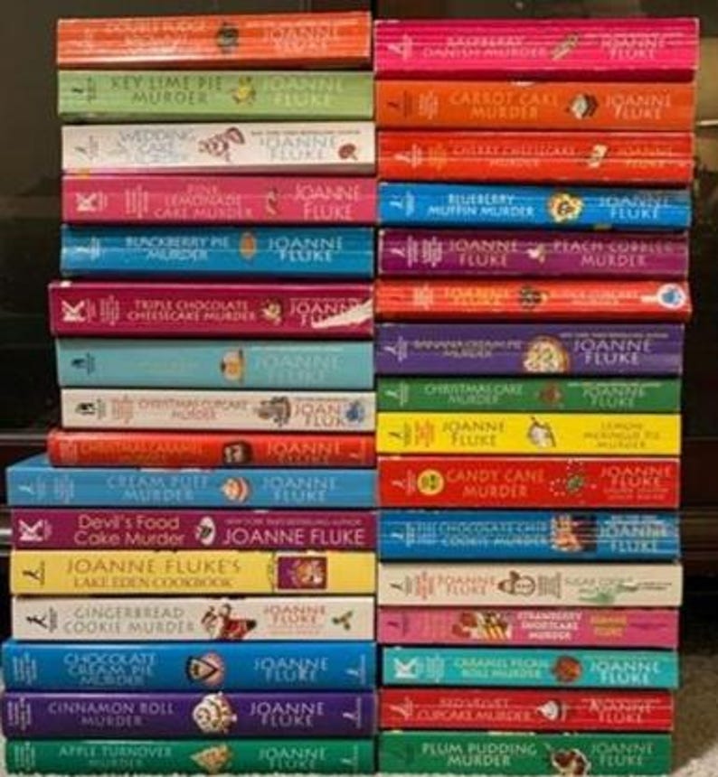 May include: A stack of colorful paperback books by Joanne Fluke, featuring titles like "Key Lime Pie Murder," "Carrot Cake Murder," and "Triple Chocolate Cheesecake Murder." The books have various colors and designs.