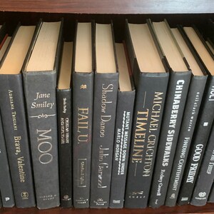 Puede incluir: Una estanter&iacute;a llena de libros negros con letras doradas. Los t&iacute;tulos incluyen "Gemba Kaizen", "Sharkman Six", "Spin Masters", "Fail U", "Shadow Dance", "Timeline", "Chinaberry Sidewalks", "Good Friday", "The Apostrophe Thief", "Rwanda, Inc.", "Vikings", "The Case for Goliath" y "Mallu Stewart".
