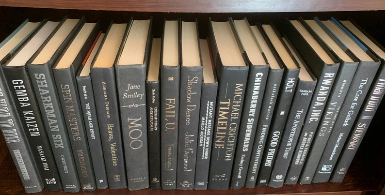 Puede incluir: Una estanter&iacute;a llena de libros negros con letras doradas. Los t&iacute;tulos incluyen "Gemba Kaizen", "Sharkman Six", "Spin Masters", "Fail U", "Shadow Dance", "Timeline", "Chinaberry Sidewalks", "Good Friday", "The Apostrophe Thief", "Rwanda, Inc.", "Vikings", "The Case for Goliath" y "Mallu Stewart".