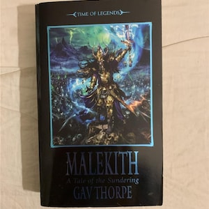 May include: A black paperback book cover with a fantasy illustration of a dark-haired warrior with a sword and blue magic. The title is "Malekith: A Tale of the Sundering" by Gav Thorpe. The book is part of the "Time of Legends" series.