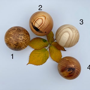 Op de afbeelding: Vier houten bollen met verschillende houtnerfpatronen. De bollen zijn genummerd van 1 tot en met 4. Een geel blad bevindt zich in het midden van de afbeelding.