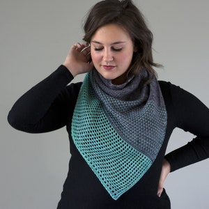 Peut inclure: Un châle triangulaire turquoise et gris avec un motif ajouré. Le châle est porté par une personne aux cheveux bruns.