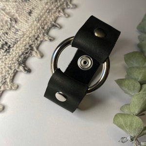 Peut inclure: Un bracelet en cuir noir avec un anneau argenté et deux clous argentés.