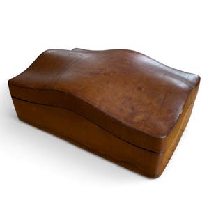 May include: A brown wooden box with a wavy, curved lid. The box has a rectangular shape with a visible seam where the lid meets the base. The wood has a natural grain and a warm, medium brown color.