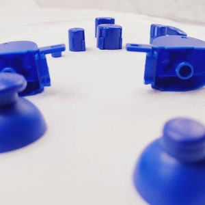 May include: A set of blue replacement buttons for a video game controller. The buttons are made of plastic and have a smooth, rounded surface.