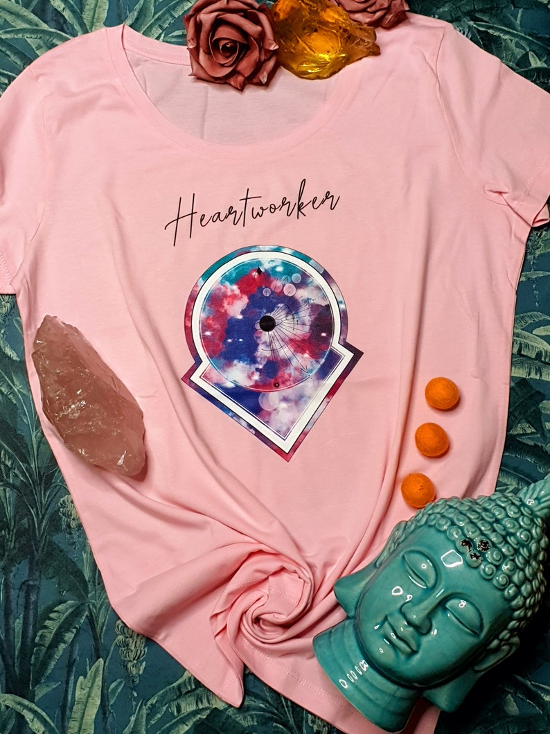 Op de afbeelding: Roze T-shirt met een grafisch ontwerp van een kleurrijke mandala met de tekst "Heartworker" gedrukt op de voorkant.