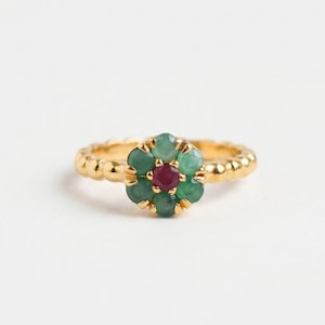May include: A gold ring with a floral design. The flower is composed of green gemstones around a central red gemstone. The ring's band has a textured, beaded pattern. The ring is a piece of jewellery.