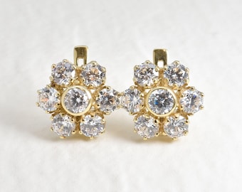 May include: A pair of gold flower-shaped earrings with clear cubic zirconia stones.