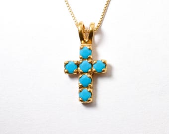 May include: A gold cross pendant with blue turquoise stones. The cross is a simple design with a smooth finish.
