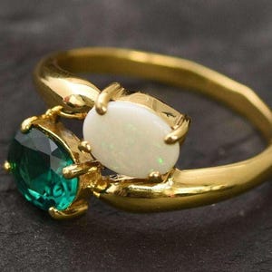 May include: A gold ring with a white opal and a green emerald stone. The stones are set in a gold band.