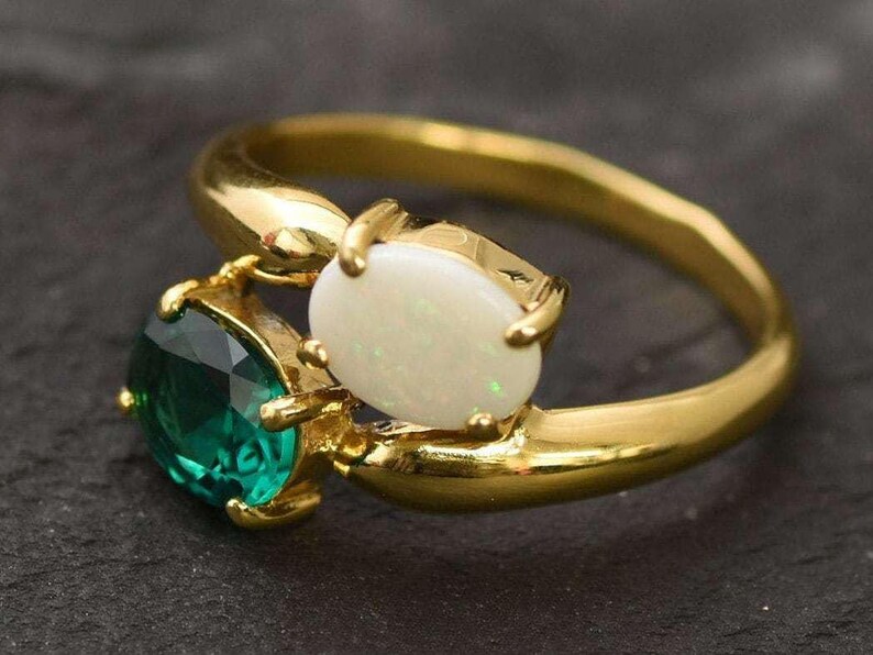 May include: A gold ring with a white opal and a green emerald stone. The stones are set in a gold band.