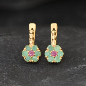 May include: A pair of gold earrings with a flower design. The earrings are made with green and pink gemstones.