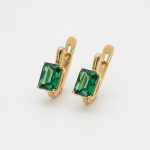May include: A pair of gold-coloured earrings, each with a rectangular, emerald-green gemstone. The earrings have a lever-back closure. The gemstones are set in a gold-coloured metal, creating a classic and elegant appearance.