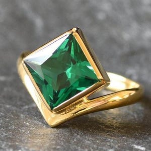 May include: A gold ring with a large, square-shaped emerald green gemstone.