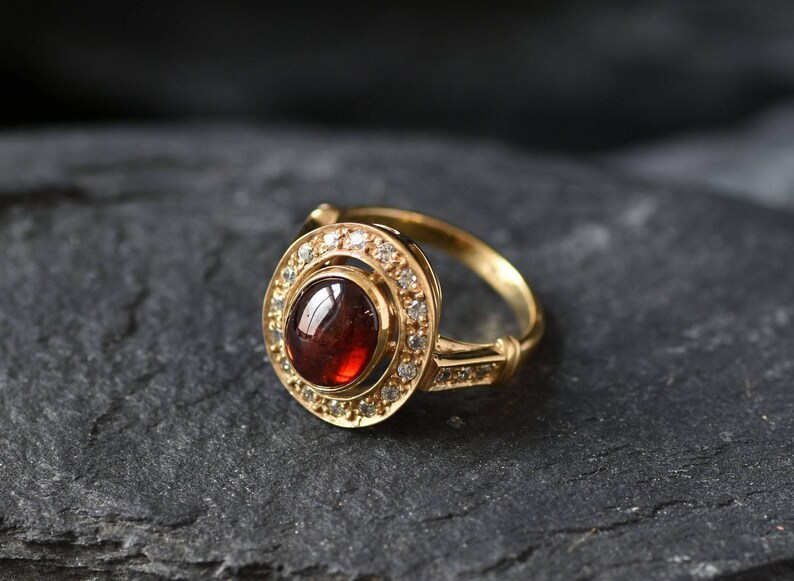 May include: A gold ring with a red gemstone surrounded by a halo of smaller white gemstones.