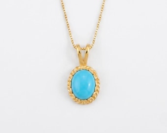 Puede incluir: Un collar de oro con una cadena fina de tipo caja y un colgante ovalado. El colgante contiene una piedra cabujón de color azul brillante y liso, engastada en un marco de oro trenzado y texturizado que combina con el acabado pulido de la cadena.