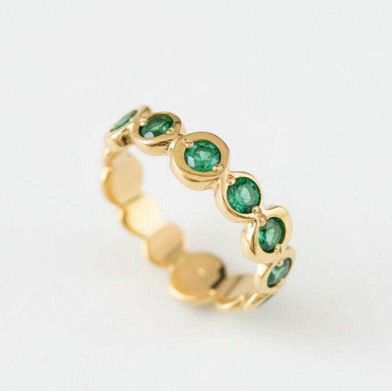 May include: A gold ring featuring a series of vibrant green gemstones. The ring's band is crafted from polished gold, with each gemstone set in a circular bezel. The gemstones are evenly spaced around the band.