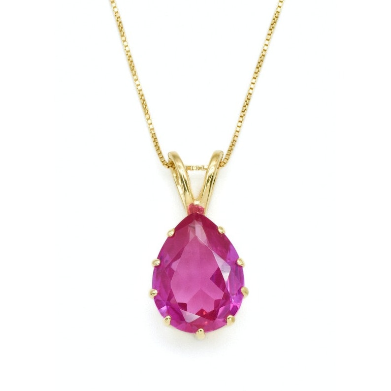 May include: A gold chain necklace with a pear-shaped pink gemstone pendant.