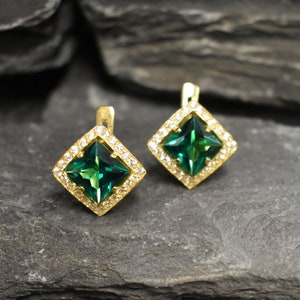 Puede incluir: Un par de pendientes de oro con piedras preciosas verdes cuadradas rodeadas de piedras preciosas transparentes m&aacute;s peque&ntilde;as.