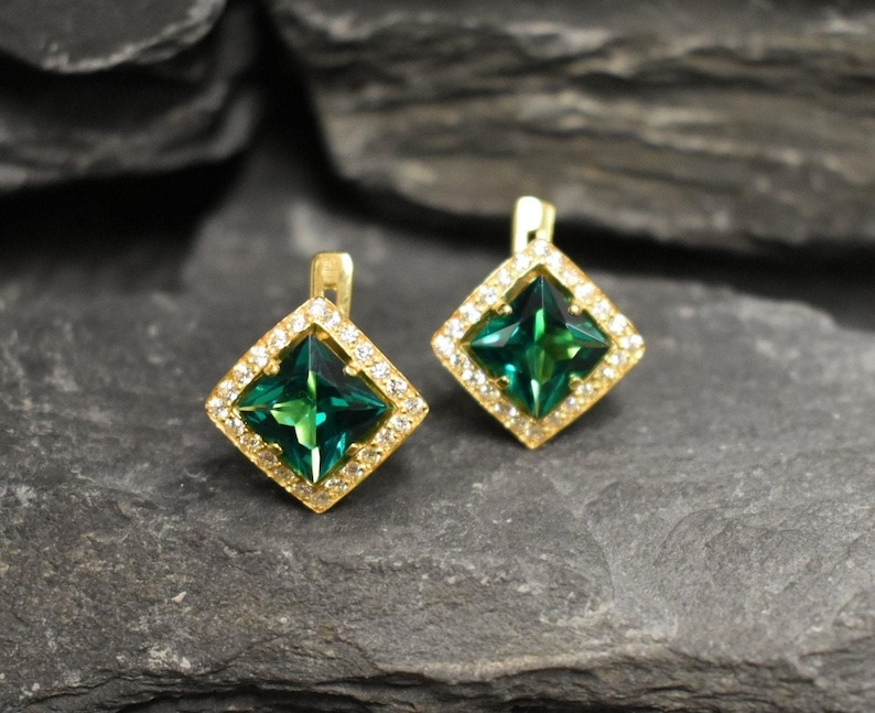 Puede incluir: Un par de pendientes de oro con piedras preciosas verdes cuadradas rodeadas de piedras preciosas transparentes m&aacute;s peque&ntilde;as.