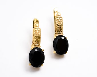 Puede incluir: Un par de pendientes de aro de oro con piedras preciosas ovaladas negras. Los pendientes tienen un diseño detallado en el aro.