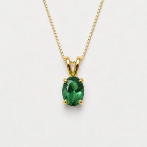 May include: A gold necklace featuring a delicate box chain and a pendant with an oval-cut green gemstone held by four prongs. The pendant is suspended from a simple gold bail, showcasing a vibrant green stone set in a polished gold metal frame.
